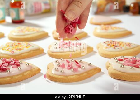 Une photo en gros plan de biscuits faits maison en forme de coeur. Les petits cœurs de confiserie sont déposés d'en haut sur l'un des biscuits. Banque D'Images