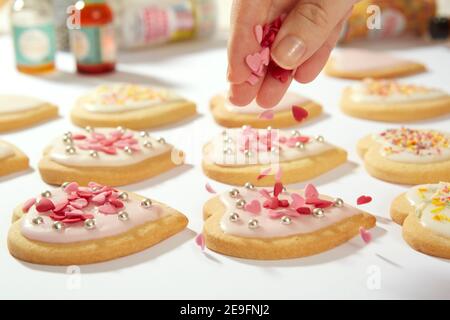 Une photo en gros plan de biscuits faits maison en forme de coeur. Les petits cœurs de confiserie sont déposés d'en haut sur l'un des biscuits. Banque D'Images