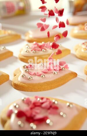 Une photo en gros plan de biscuits faits maison en forme de coeur. Les petits cœurs de confiserie sont déposés d'en haut sur l'un des biscuits. Banque D'Images