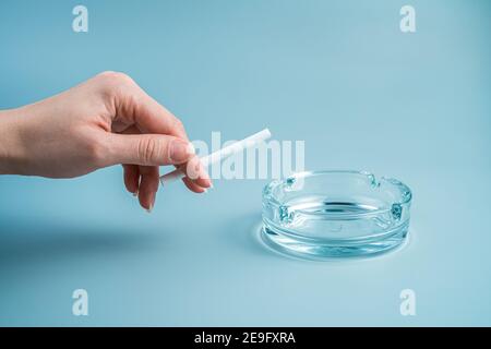 La main d'une femme casse une cigarette sur un fond bleu clair. Vue latérale avec espace de copie. Banque D'Images