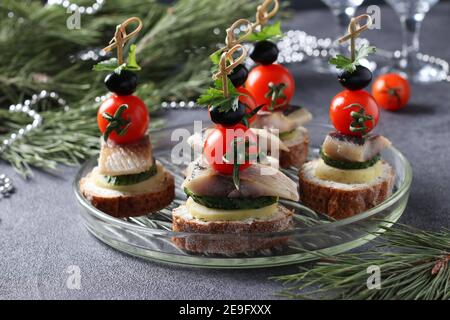 Canape avec hareng salé, concombre, pommes de terre bouillies, tomates cerises et olives noires sur croûtons de seigle sur fond gris. Gros plan Banque D'Images