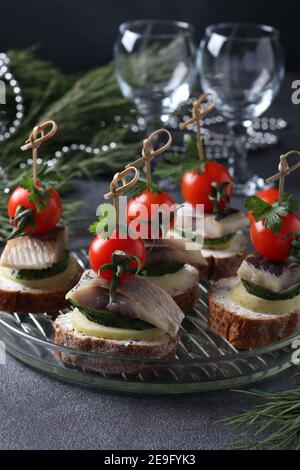 Canape avec hareng salé, concombre, pommes de terre bouillies, tomates cerises et olives noires sur croûtons de seigle sur fond gris. Format vertical Banque D'Images