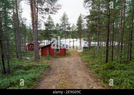 Magnifique cabine en bois rouge isolée en Inari, Laponie, Finlande. Le rondin est entouré d'une forêt de pins verts idyllique et d'un lac romantique dans le désert Banque D'Images