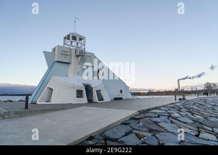 Vue latérale du phare de Nallikari à Oulu, Finlande, sur la mer Baltique. Tour maritime à l'extrémité de la jetée pavée avec fumée d'une usine dans l'arrière-gro Banque D'Images