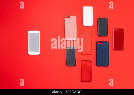 Choix de housses arrière en plastique multicolore pour téléphones portables sur arrière-plan rouge avec un smartphone sur le côté Banque D'Images