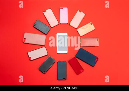 Choix de housses arrière en plastique multicolore pour téléphones portables sur arrière-plan rouge avec un smartphone sur le côté Banque D'Images