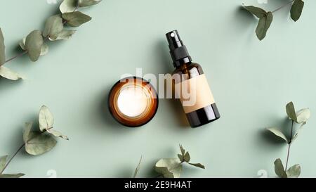 Maquette de marque de PRODUITS COSMÉTIQUES SPA. Pot de crème hydratante et bouteille en verre ambré vaporisée sur fond vert avec feuilles d'eucalyptus. Herbe biologique Banque D'Images