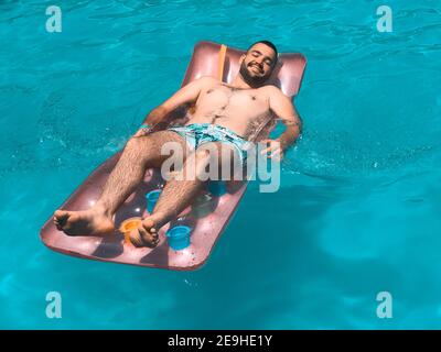 Homme adulte allongé sur un matelas pneumatique au bord d'une piscine sous la lumière du soleil en été Banque D'Images