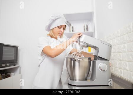 Cuisine, pâtisserie, confiserie. Jolie jeune femme confiseur fouetter des blancs d'oeufs avec du sucre dans un mélangeur planétaire, préparant le merengue pour Banque D'Images