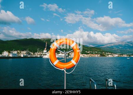 Bouée de sauvetage orange sur un stand en métal sur fond de montagnes, d'eau et de ciel. Banque D'Images