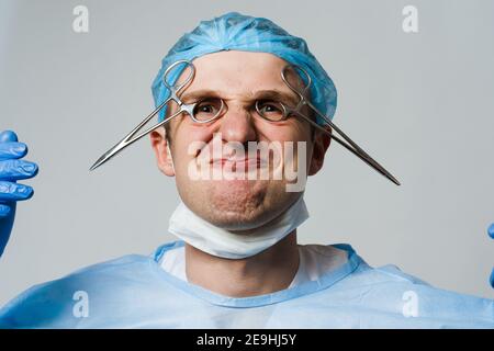 Un médecin chirurgien souriant et enragnant avec des émotions folles. Jeune médecin tenant des ciseaux médicaux Banque D'Images