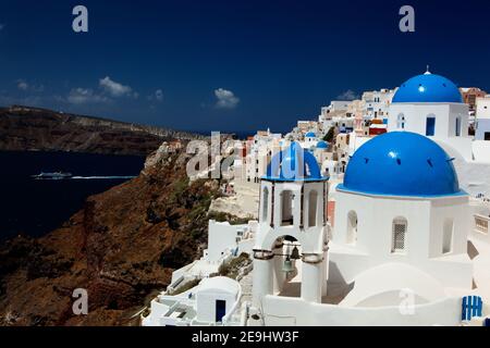 Santorini, Grèce l'église en dôme bleu et le village blanc d'Oia sur la falaise donnent sur un ferry dans la Caldera. Banque D'Images