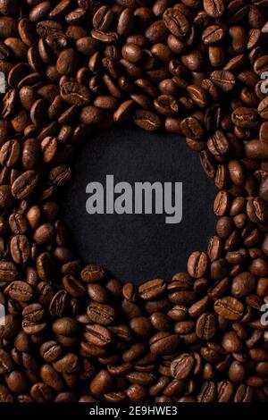 Grains de café fraîchement torréfiés sur fond de pierre noire. Placez le texte sous forme de cercle. Vue de dessus, plan d'affichage avec espace de copie Banque D'Images