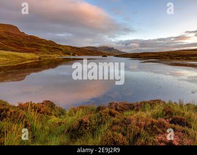 Île de Skye, Écosse : lumière du lever du soleil et nuages se reflétant dans le Loch Fada avec des bruyères qui fleurissent sur le rivage et l'emblématique Old Man of Storr dans le Th Banque D'Images