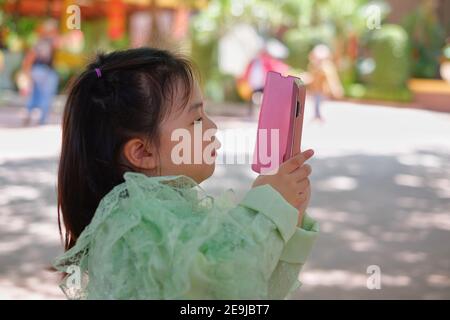 Une jolie jeune fille asiatique tient un smartphone rose, essayant de prendre une photo pendant ses vacances. Banque D'Images