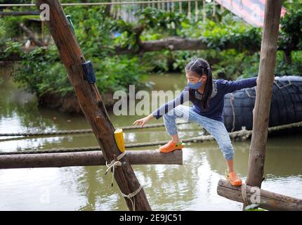 Une jolie jeune fille asiatique essayant de traverser un petit canal à travers une structure en bois avec des trous d'ouverture, en étant courageuse mais prudente pour atteindre sa destination. Banque D'Images