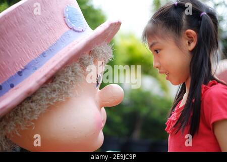 Vue latérale d'une jeune fille asiatique mignonne ayant un visage à visage regardant une statue, jouant et s'amusant. Banque D'Images