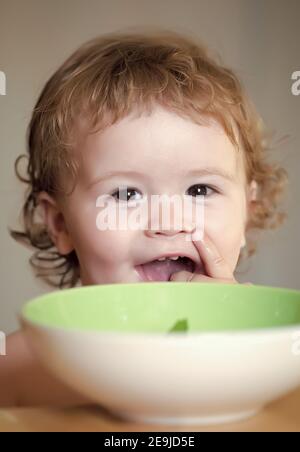 Repas de bébé, repas d'enfant mignon. Portrait d'un adorable enfant souriant mangeant de l'assiette à la main. Banque D'Images