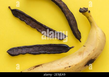 Banane mûre et fruit de caroube, sur fond jaune Banque D'Images