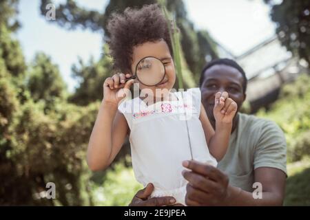 Petite fille aux cheveux bouclés tenant une loupe et regardant à travers elle Banque D'Images