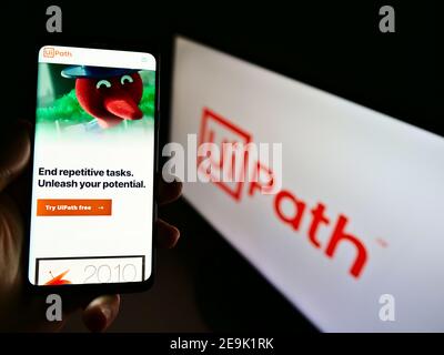 Personne tenant un téléphone mobile avec le site Web de la société de développement de logiciels UiPath Inc. Exposé devant le logo. Mise au point au centre de l'écran du téléphone. Banque D'Images