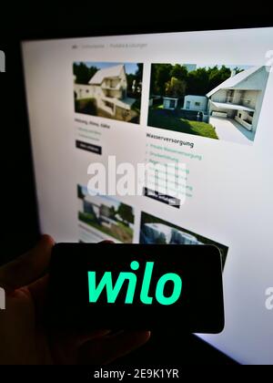 Personne portant un smartphone avec le logo du fabricant allemand de systèmes de pompe Wilo se affiché devant la page Web d'affaires. Mise au point sur l'écran du téléphone. Banque D'Images