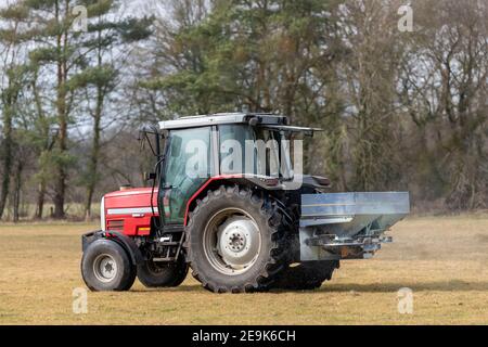 Tracteur rouge sur un pâturage avec un épandeur de chaux Le début du printemps aux pays-Bas Banque D'Images