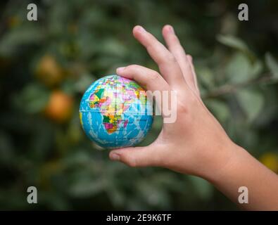 Petit globe miniature coloré dans la main d'un enfant un arrière-plan vert Banque D'Images