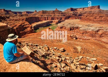 Un homme assis sur le fleuve Colorado surplombe dans la région de Walking Rocks, Dead Horse point falaises in distance, White Rim Road, Parc national de Canyonlands, Utah USA Banque D'Images