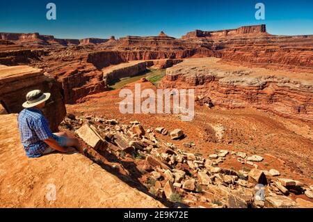 Un homme assis sur le fleuve Colorado surplombe dans la région de Walking Rocks, Dead Horse point falaises in distance, White Rim Road, Parc national de Canyonlands, Utah USA Banque D'Images