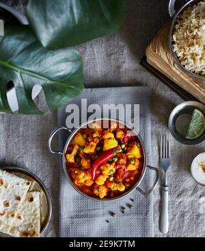 Aloo gobi cuisine traditionnelle indienne à base de chou-fleur et de pommes de terre décorée de piment rouge servi avec du riz brun, du dahi, de l'eau de citron et du chapati sur la ta Banque D'Images