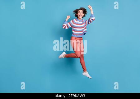 Photo de la taille du corps pleine longueur de saut gaiement jeune fille des gestes comme un gagnant isolé sur un arrière-plan bleu vif Banque D'Images