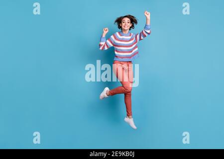 Pleine longueur de la photo de corps de saut heureusement jeune fille vêtu d'un chandail rayé isolé sur fond bleu vif Banque D'Images