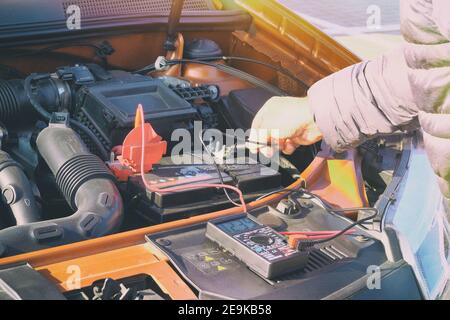 Mesure de la tension de la batterie dans une voiture. Inspection du conducteur tenant le voltmètre du testeur de capacité de la batterie. Image en tons. Banque D'Images