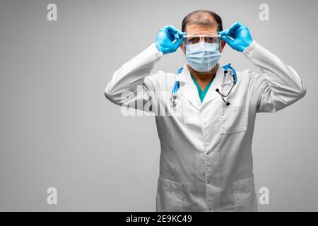 Homme d'âge moyen médecin mettant sur un écran facial, fond gris Banque D'Images