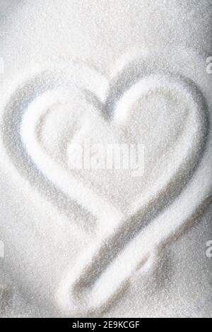 Forme de coeur dessinant du sucre blanc sur fond de sucre granulé. Banque D'Images