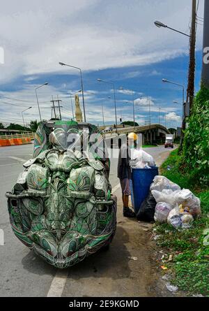 Un vieil homme asiatique se ruant dans une poubelle, collectant des articles recyclables dans sa main de véhicule personnalisée en plastique recyclé. Banque D'Images