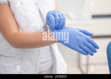 Une femme médecin méconnaissable met des gants en caoutchouc, travaillant à l'hôpital Banque D'Images