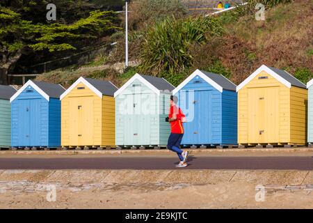 Bournemouth, Dorset, Royaume-Uni. 5 février 2021. Météo au Royaume-Uni : le soleil chaud s'est envengé avec des douches sur les plages de Bournemouth tandis que les gens se dirigent vers le bord de mer pour leur exercice quotidien pendant le Lockdown 3 de l'épidémie pandémique du coronavirus Covid 19 Covid19 du virus Corona. Des pistes de jogging Man JOGS longent la promenade et longent des cabanes de plage. Crédit : Carolyn Jenkins/Alay Live News Banque D'Images