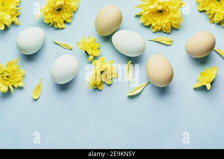 Concept de Pâques. Œufs et chrysanthèmes jaunes fleurs sur fond bleu. Maquette. Carte de vacances joyeuses Pâques du printemps. Vue de dessus. Banque D'Images