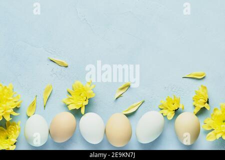 Concept de Pâques. Œufs et chrysanthèmes jaunes fleurs sur fond bleu. Maquette. Carte de vacances joyeuses Pâques du printemps. Vue de dessus. Banque D'Images