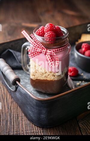 Dessert sans cuisson avec mousse au chocolat noir, biscuits écrasés et fromage à la crème à la framboise dans un pot en verre sur fond de bois rustique Banque D'Images