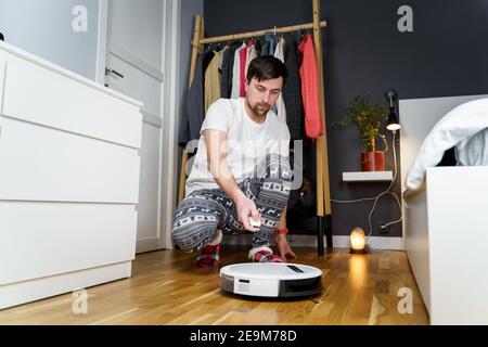 Jeune homme caucasien faisant le nettoyage pour les vacances de noël en hiver. Un homme en drôle de vêtements de maison, pyjama avec ornement d'hiver collecte et ensembles Banque D'Images