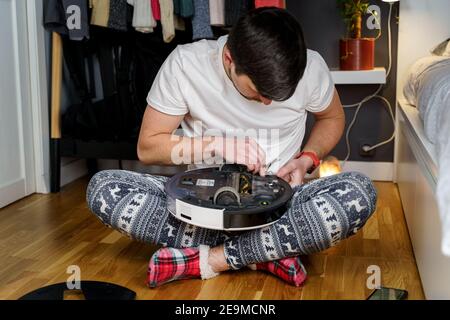 Jeune homme caucasien faisant le nettoyage pour les vacances de noël en hiver. Un homme en drôle de vêtements de maison, pyjama avec ornement d'hiver collecte et ensembles Banque D'Images