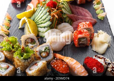 Ensemble de sushis avec noix de Saint-Jacques et légumes, sur pierre noire, sur fond blanc Banque D'Images