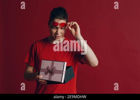 Adorable gars avec boîte cadeau sur fond rouge. Banque D'Images