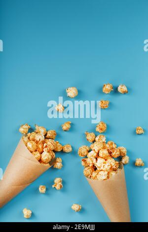 Pop-corn au caramel dans une enveloppe en papier sur fond bleu. Félicitations pour avoir regardé des films, des séries, des dessins animés. Espace libre, vue de dessus. Banque D'Images