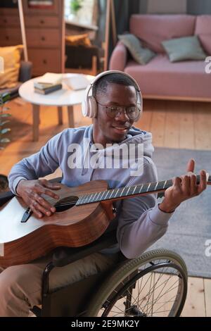 Homme africain handicapé assis sur un fauteuil roulant et jouant de la guitare dans la chambre Banque D'Images