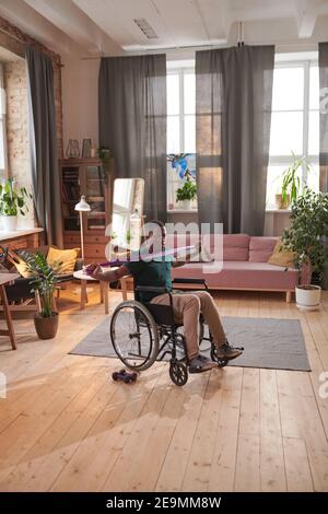 Homme africain assis en fauteuil roulant et faisant de l'exercice à la maison pendant sa récupération Banque D'Images