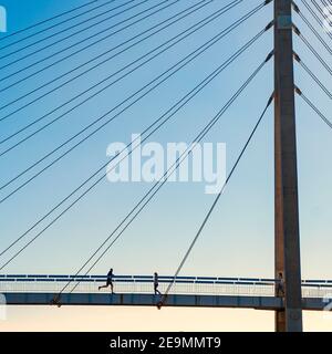 Un homme court dans une femme sur un pont suspendu en face de la mer lors d'une journée d'hiver ensoleillée à Fuengirola. Banque D'Images